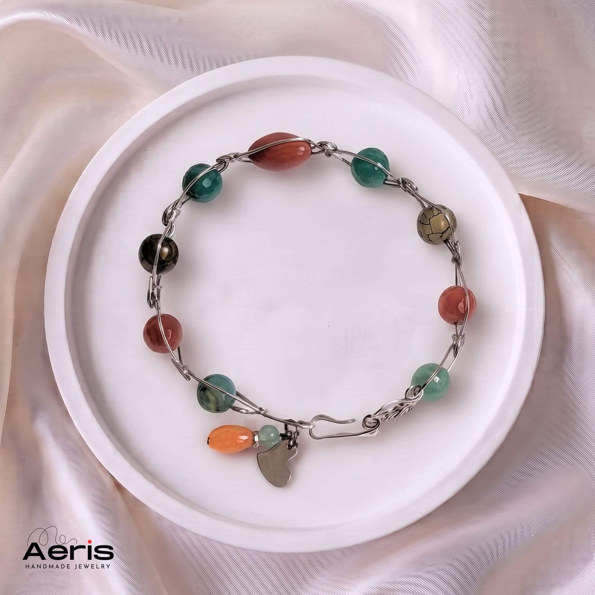 Bratara fixa cu agate multicolore si sarma din inox, asezata pe un vas ceramic
