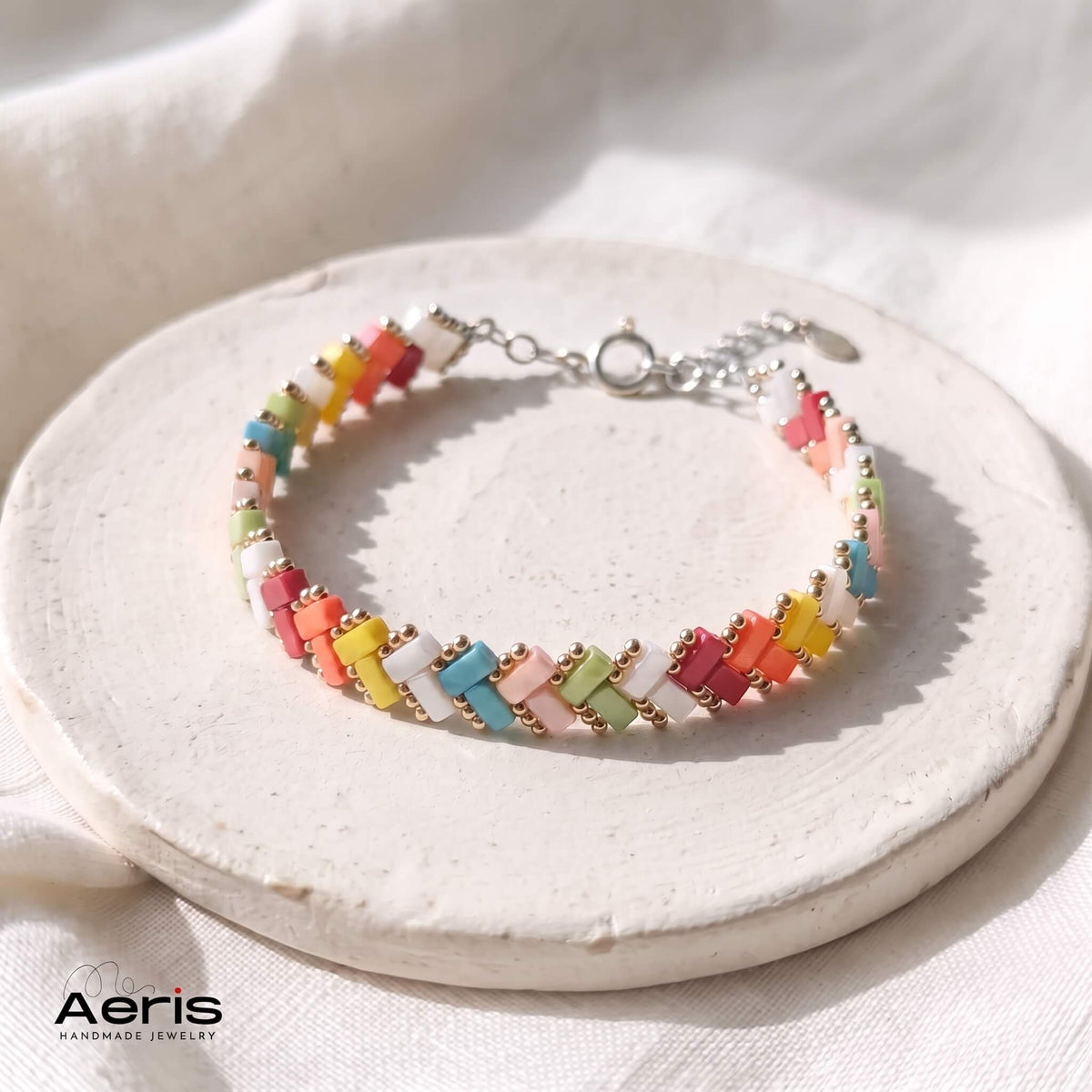 Bratara handmade din margele Miyuki in culorile curcubeului si cu finisaje din inox, prezentata pe un soclu rotund ceramic
