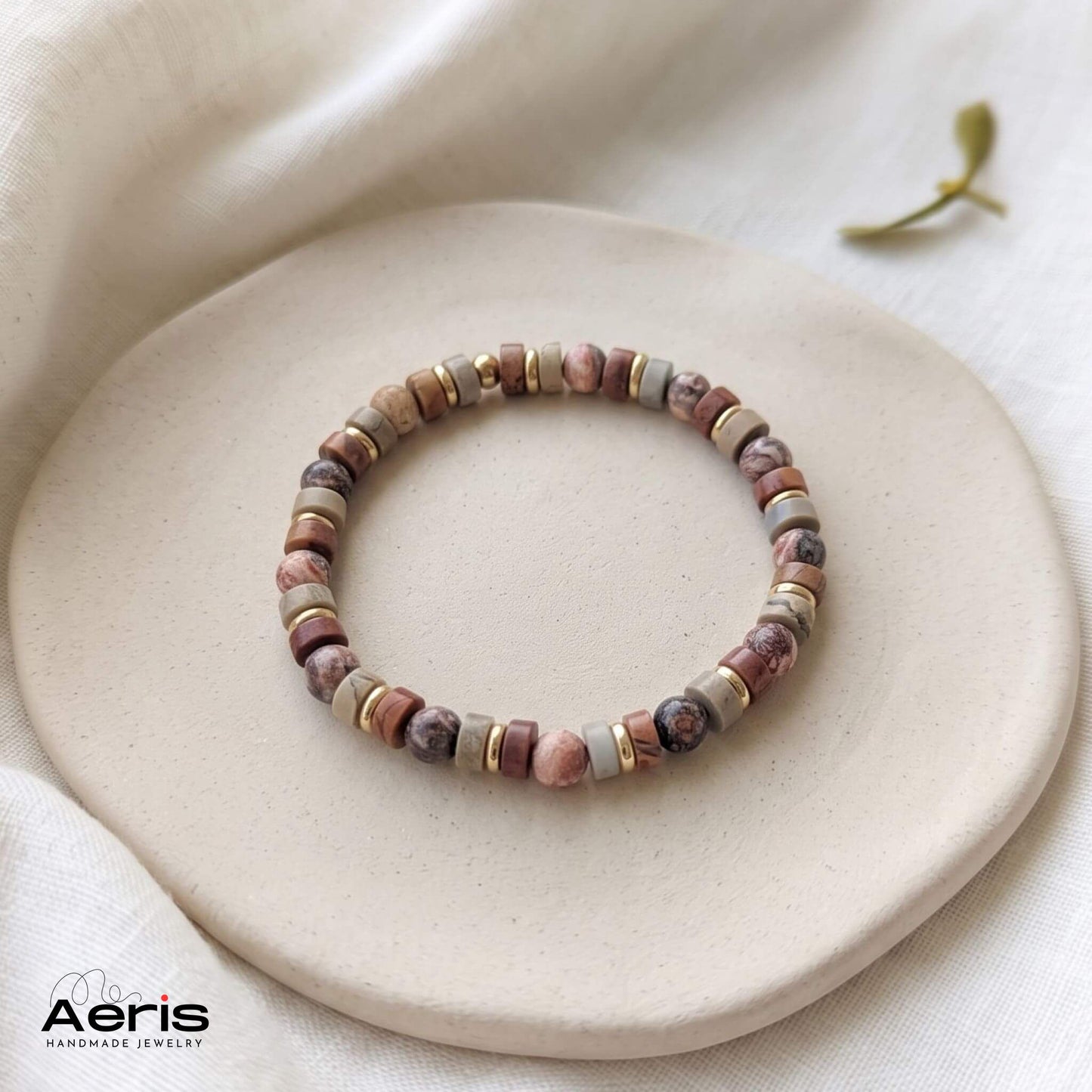 Bratara handmade unisex, in nuante neutre, expusa pe un soclu din ceramica mata