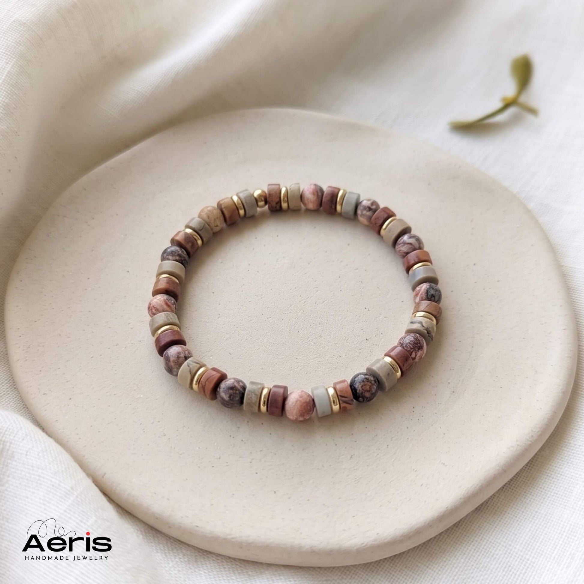 Bratara handmade unisex, in nuante neutre, expusa pe un soclu din ceramica mata