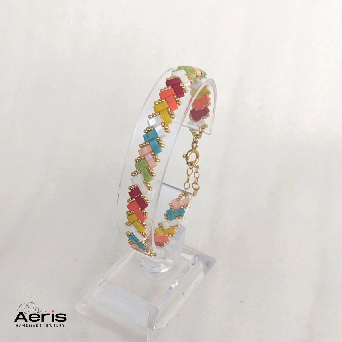 Bratara handmade din margele Miyuki in nuante de curcubeu, asezata pe un suport acrilic transparent