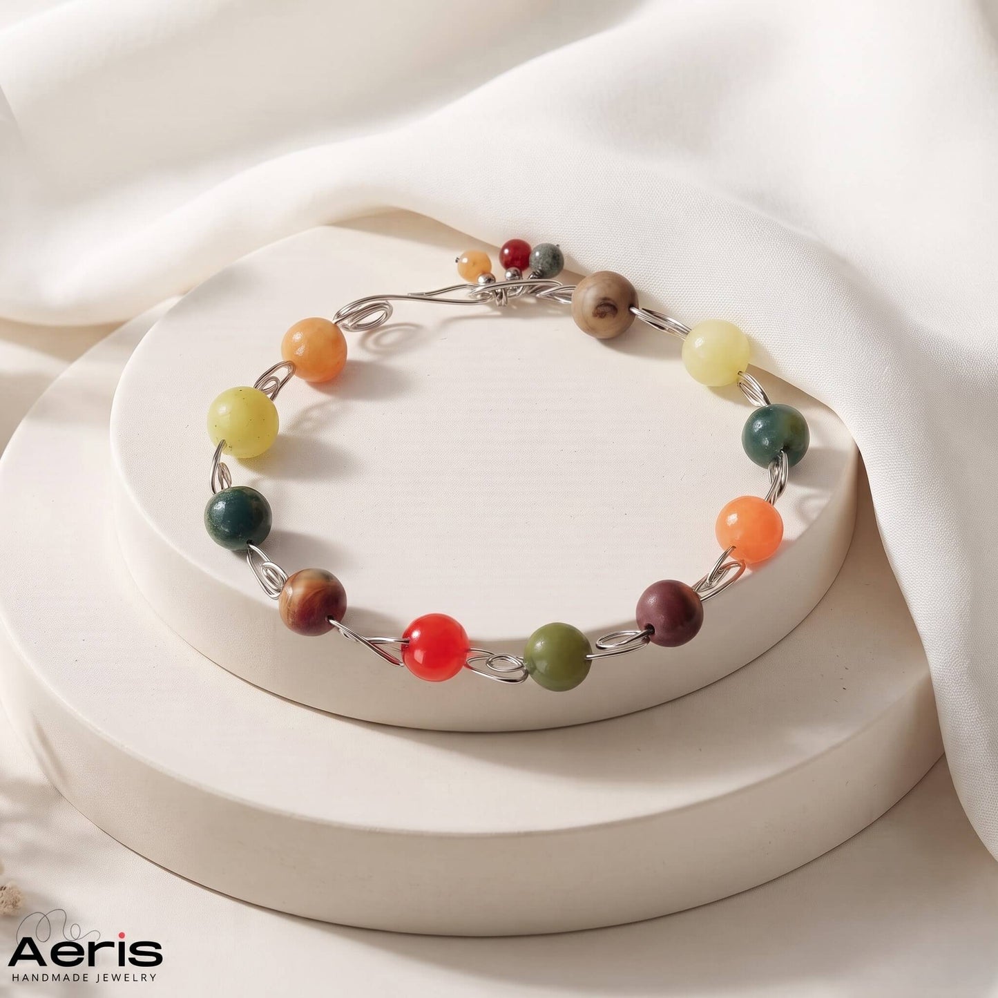 Bratara handmade din sarma de inox si agate colorate, prezentata pe un suport ceramic