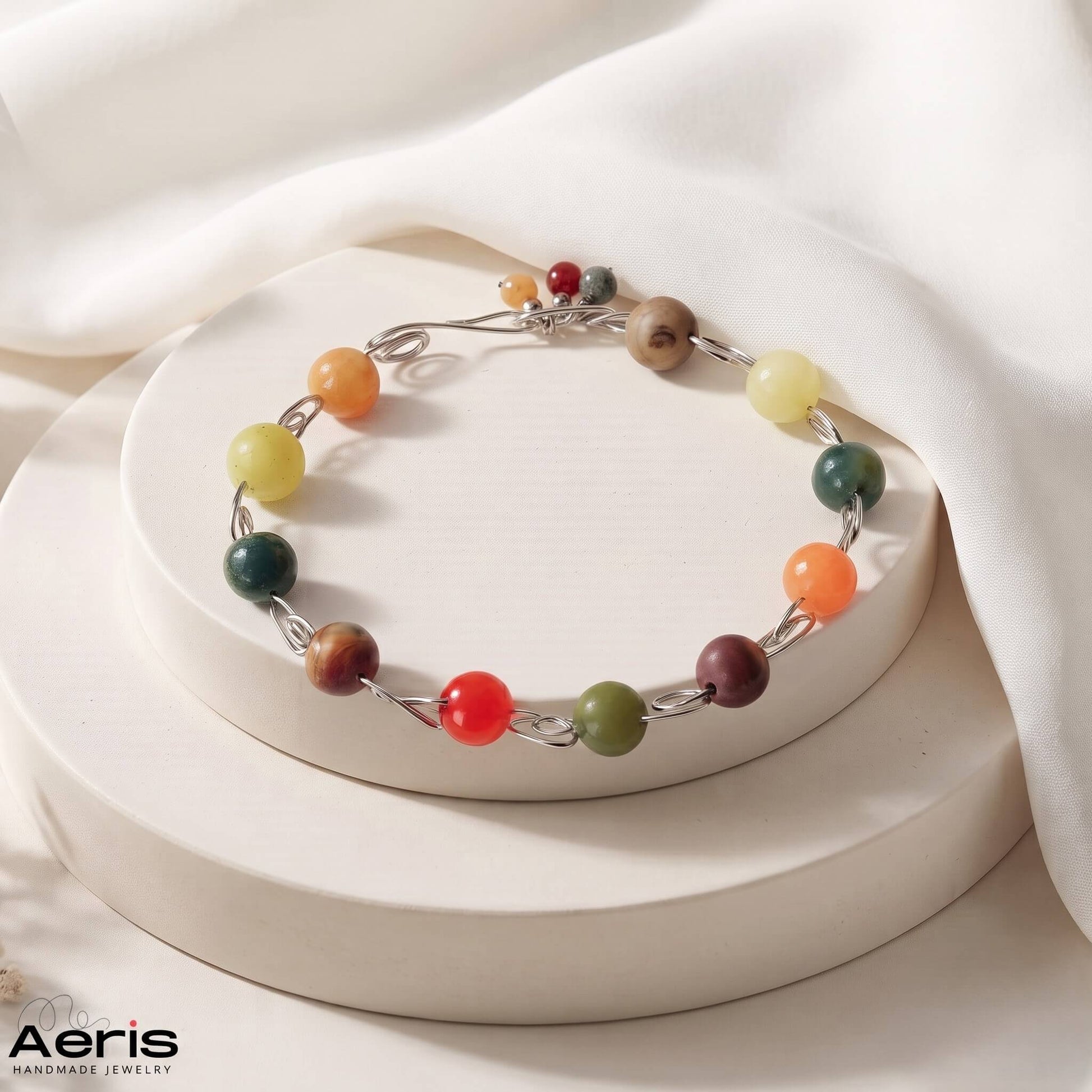 Bratara handmade din sarma de inox si agate colorate, prezentata pe un suport ceramic
