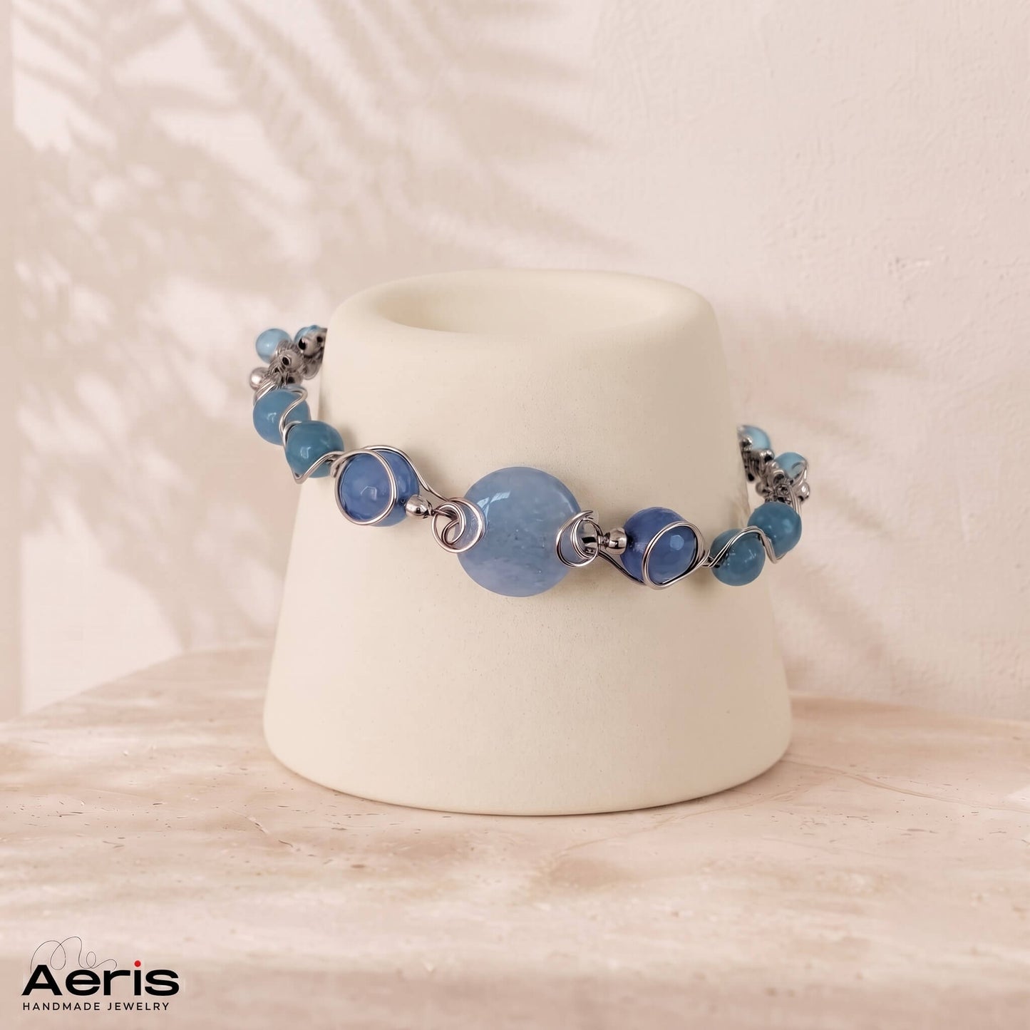 Bratara lucrata in tehnica wire wrapping cu sarma din inox si pietre semipretioase bleu, prezentata pe un suport ceramic