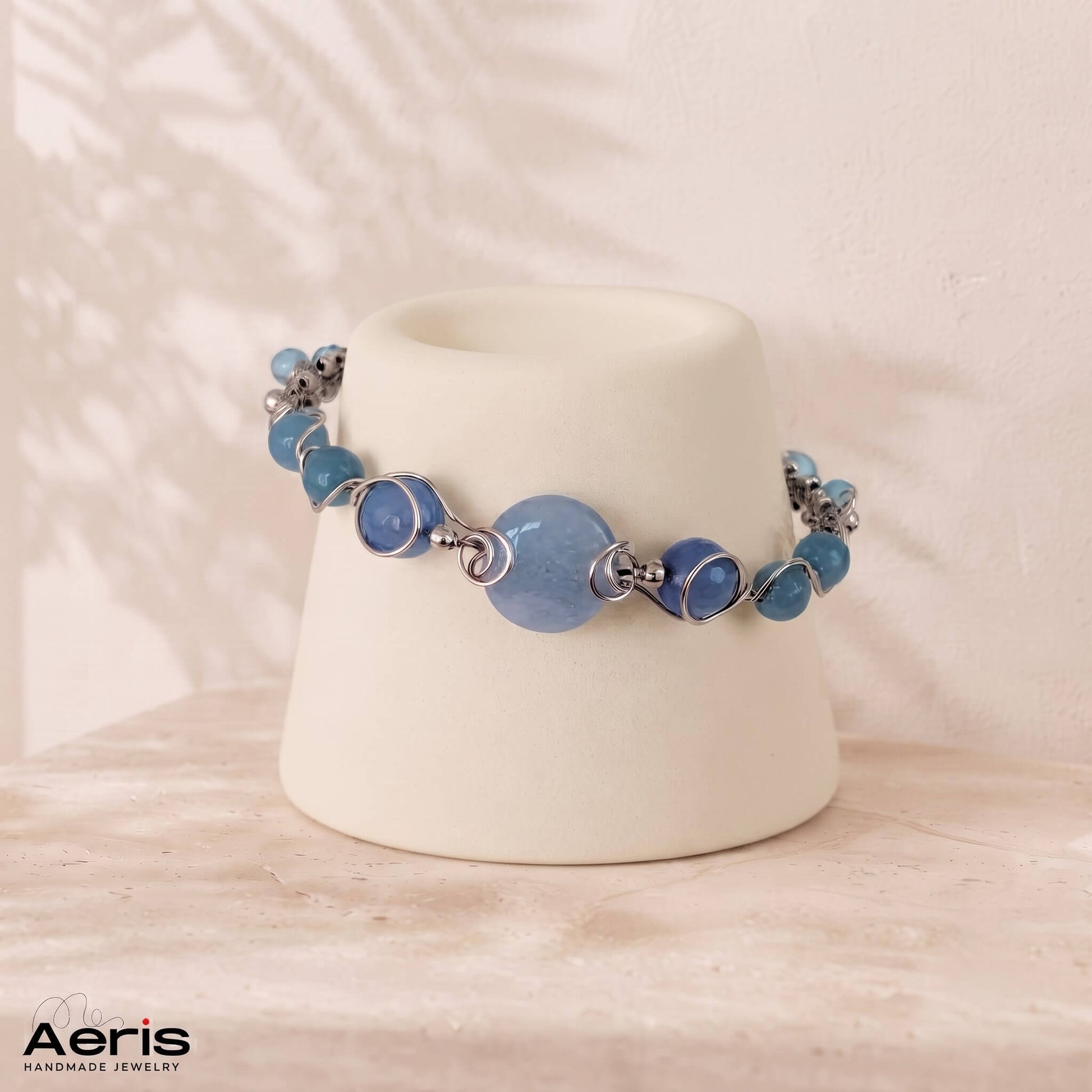 Bratara lucrata in tehnica wire wrapping cu sarma din inox si pietre semipretioase bleu, prezentata pe un suport ceramic