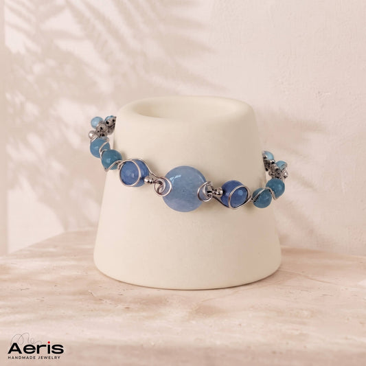 Bratara lucrata in tehnica wire wrapping cu sarma din inox si pietre semipretioase bleu, prezentata pe un suport ceramic