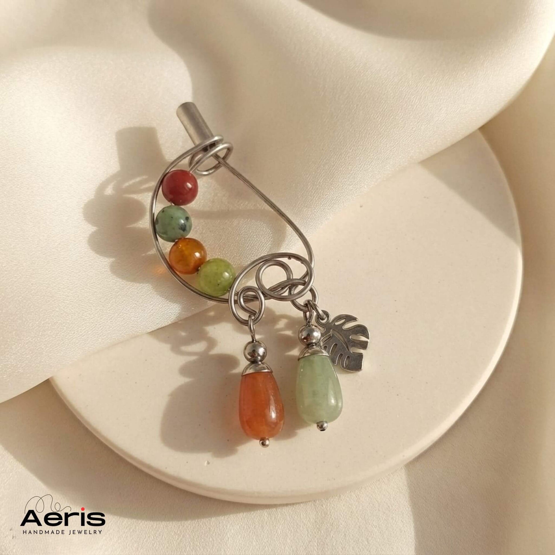 Brosa din sarma de inox modelata artistic, cu pietre semipretioase, expusa pe un suport rotund ceramic