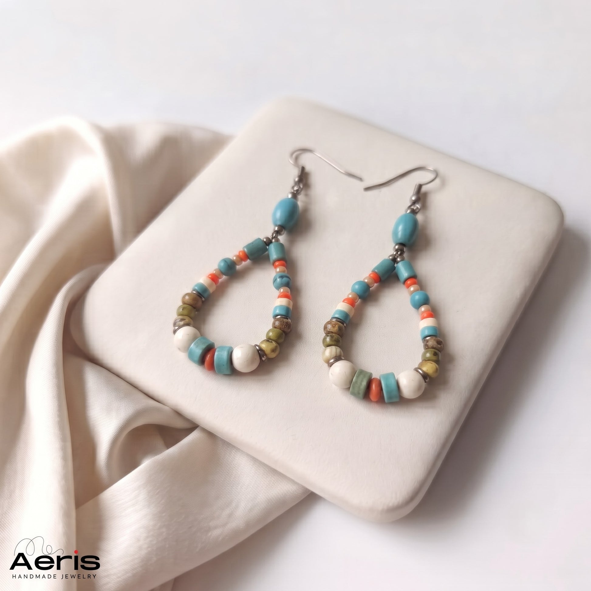 Cercei boho-chic din margele semipretioase, prezentati pe un suport patrat din ceramica mata