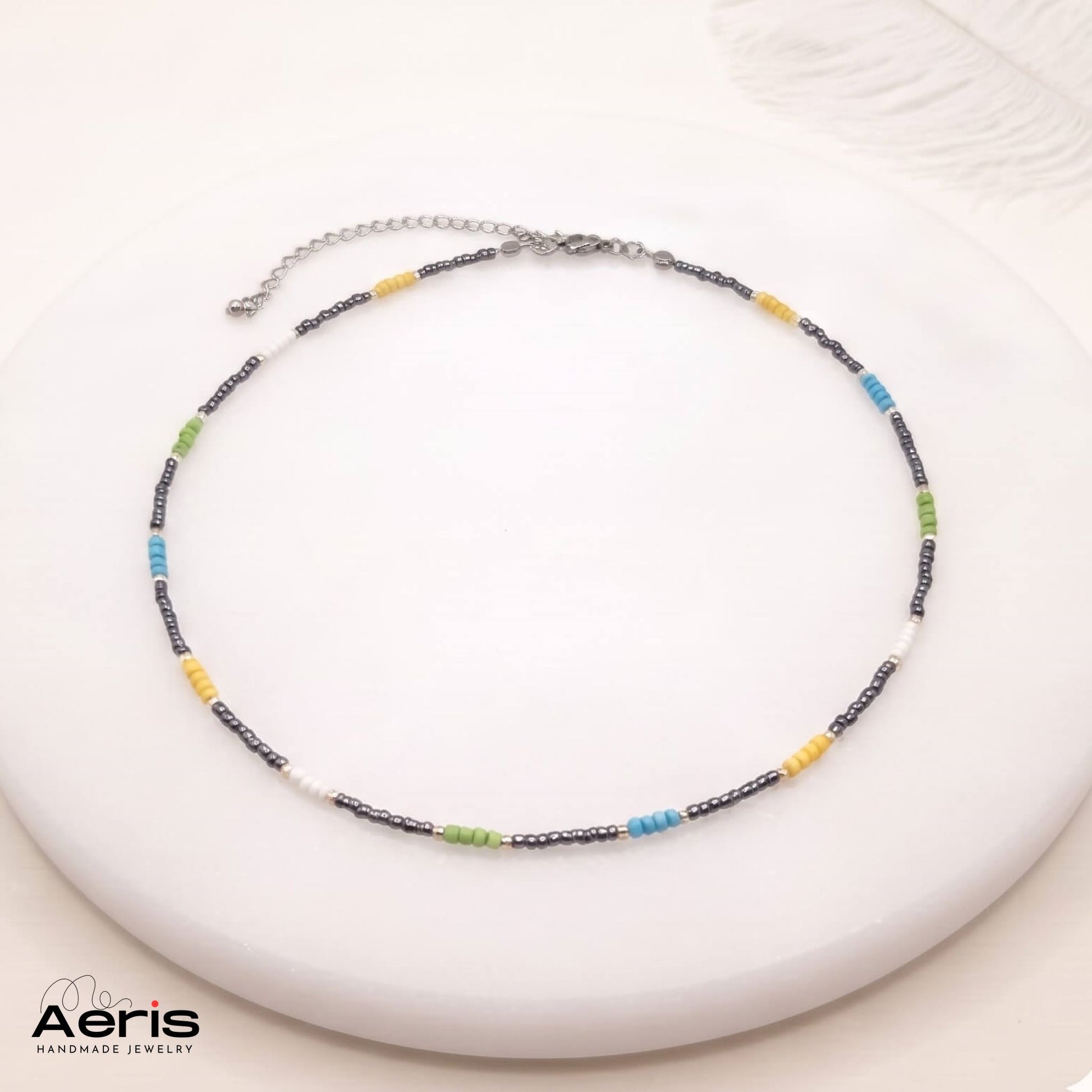 Choker multicolor din margele de nisip, expus pe un soclu din ceramica
