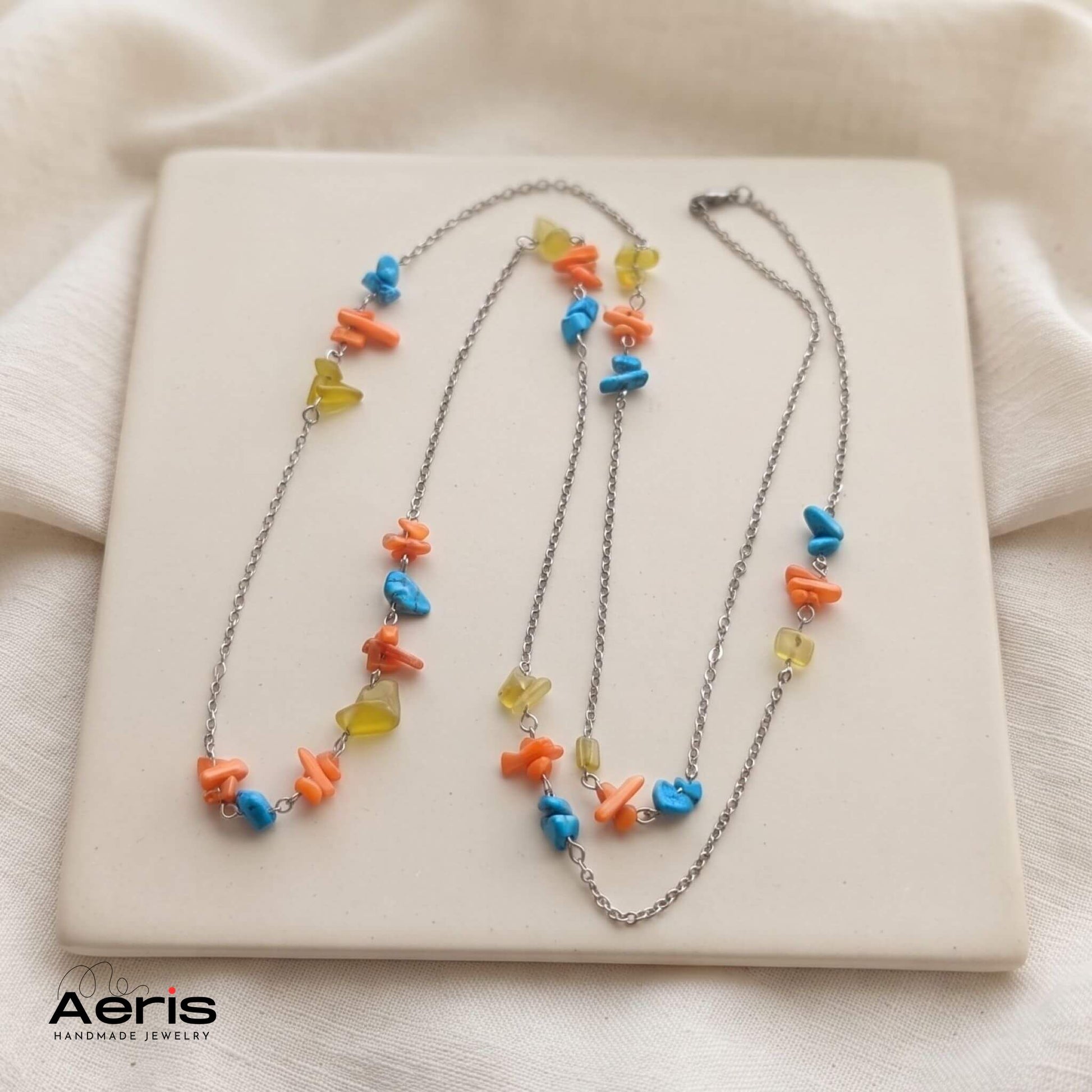 Colier handmade din lant de inox si chipsuri colorate, expus pe o placa ceramica patrata