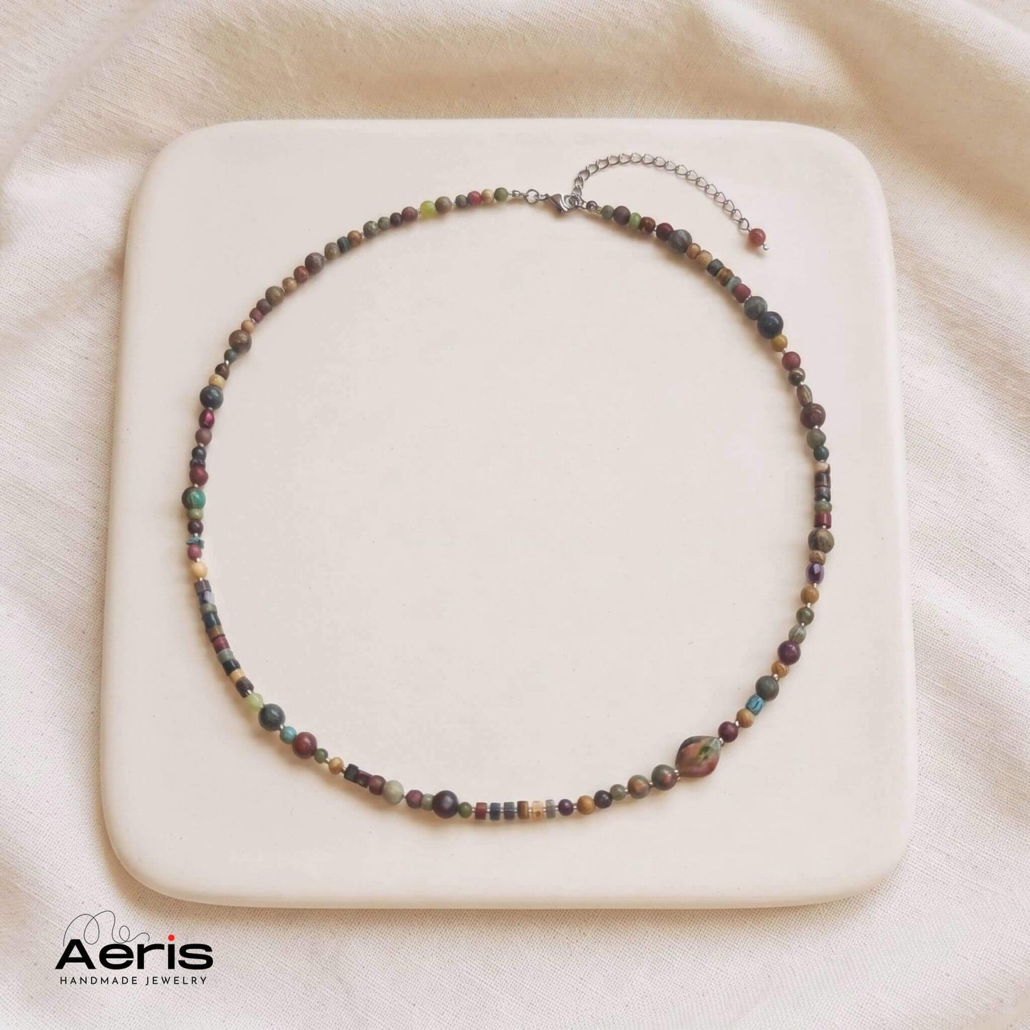 Colier boho-chic multicolor, asezat pe o placa ceramica patrata