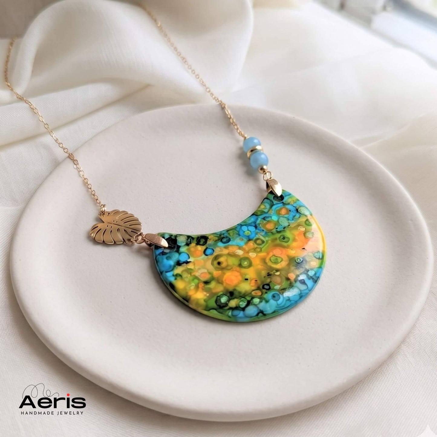 Colier handmade cu margele din angelit si elemente decorative din inox auriu, asezat pe un suport ceramic
