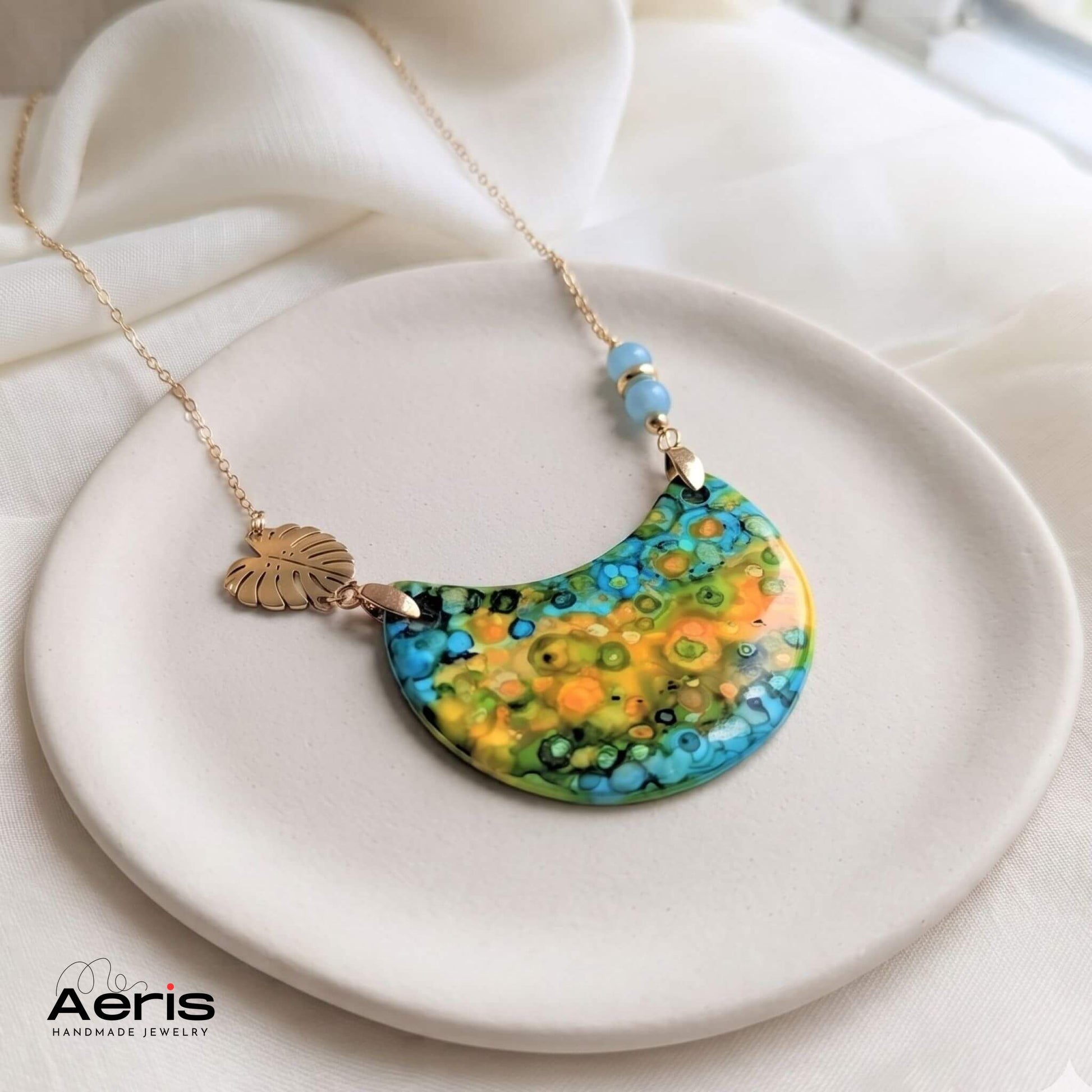 Colier handmade cu margele din angelit si elemente decorative din inox auriu, asezat pe un suport ceramic