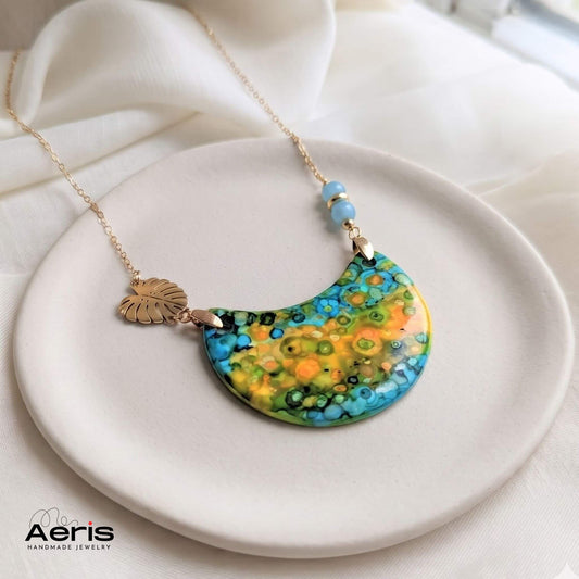Colier handmade cu margele din angelit si elemente decorative din inox auriu, asezat pe un suport ceramic