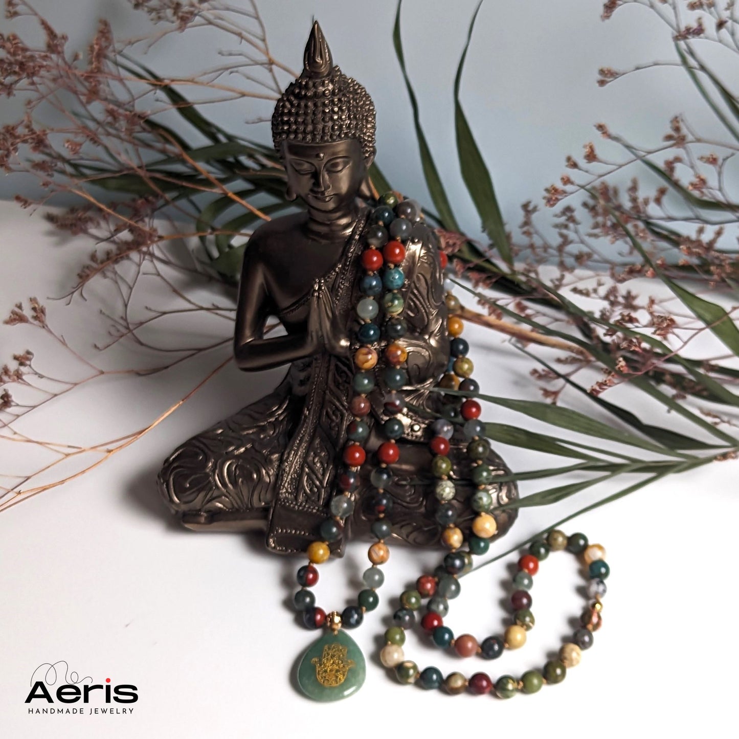 Colier handmade multicolor din margele semipretioase, asezat langa statuia lui Buddha