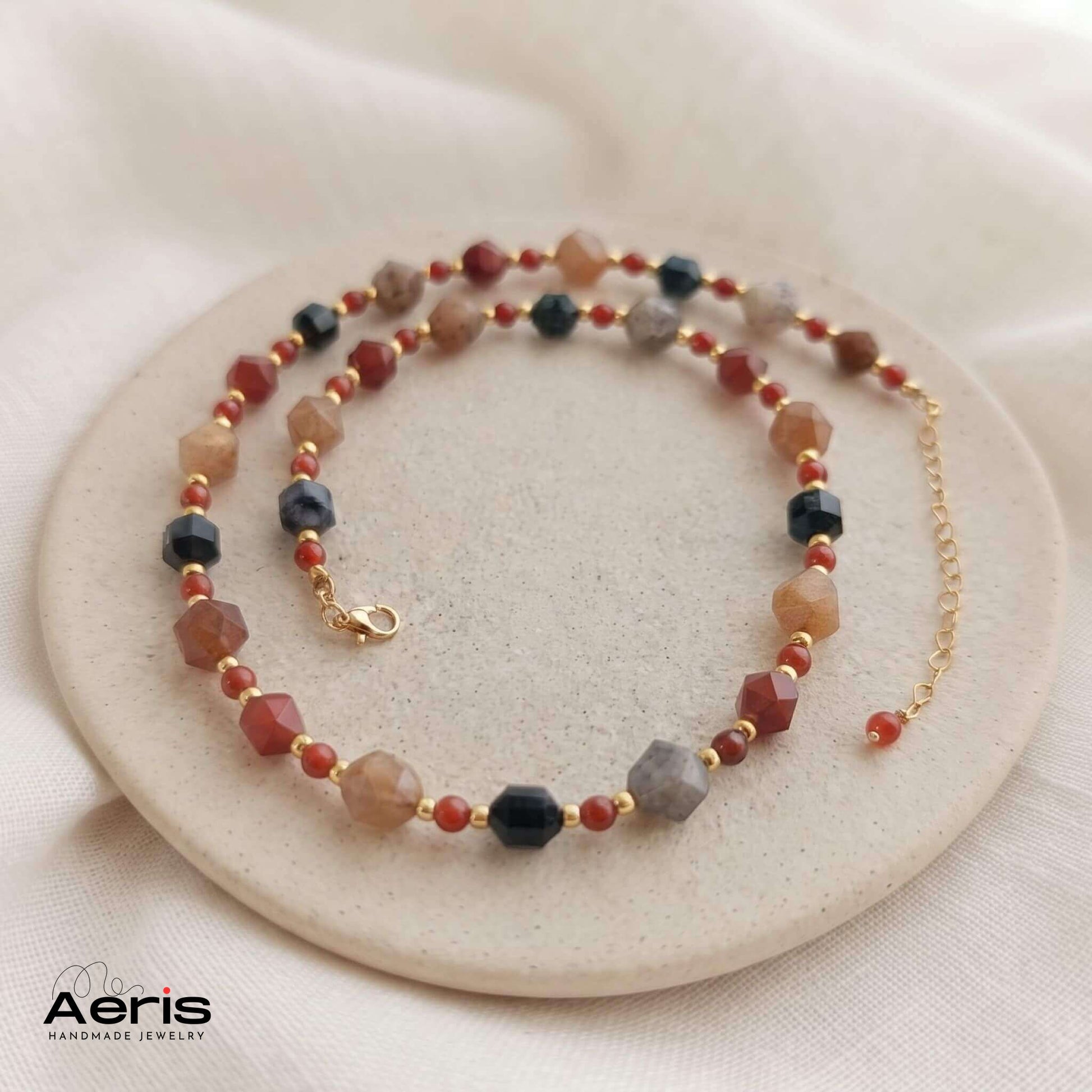Colier elegant cu agate multicolore si carneol, expus pe un soclu din ceramica mata