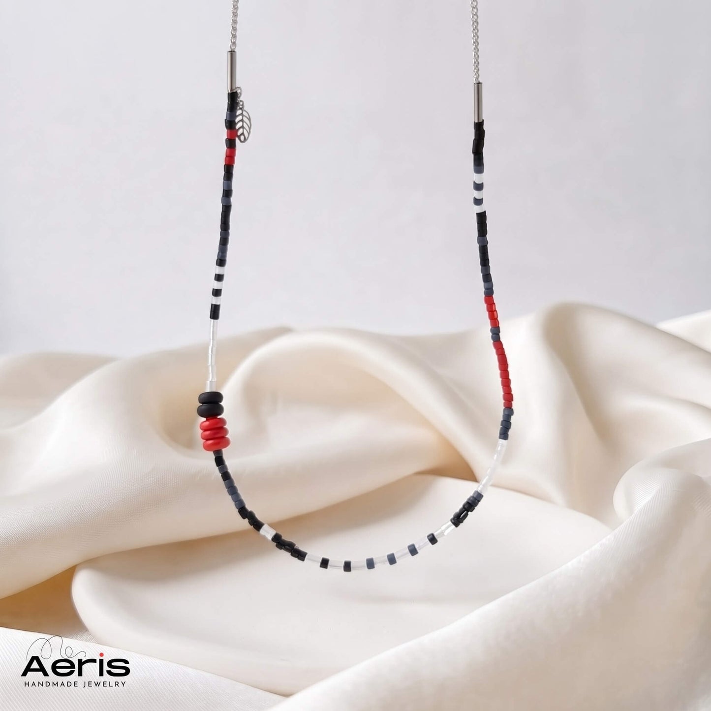 Colier handmade in alb, rosu si negru, suspendat deasupra unui disc ceramic