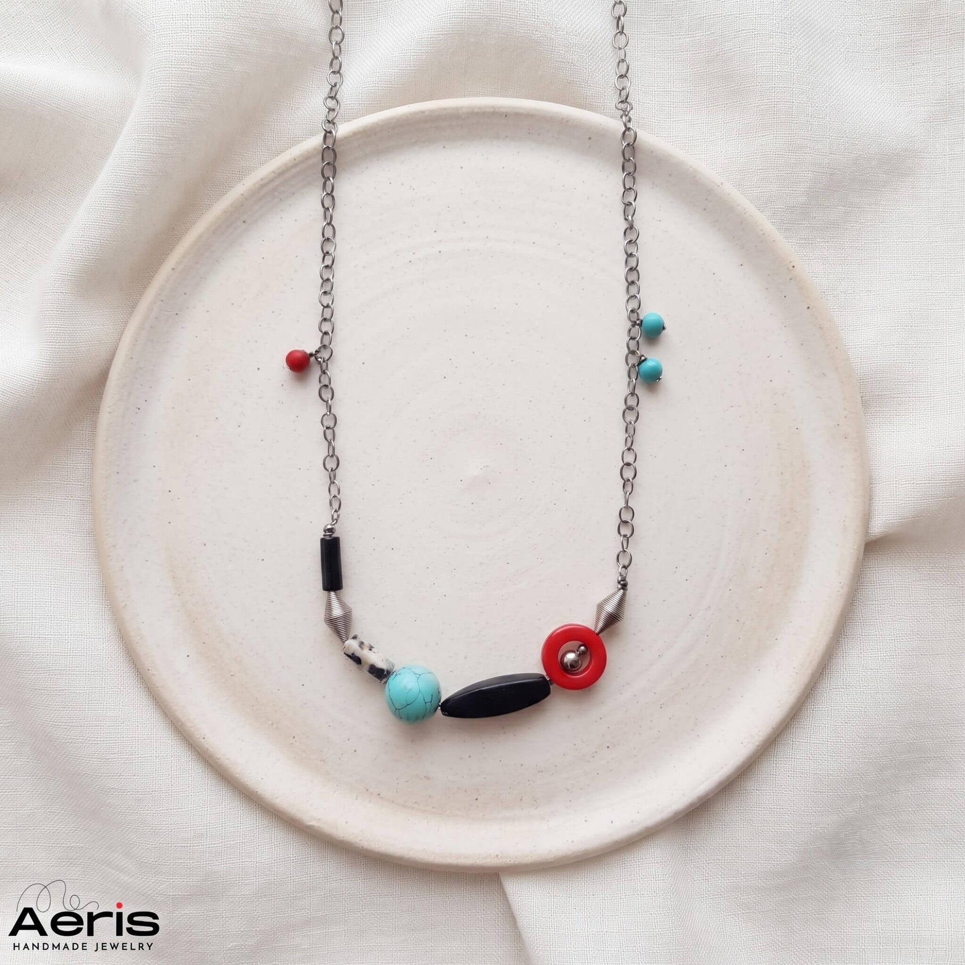 Colier handmade asimetric, asezat pe un platou ceramic