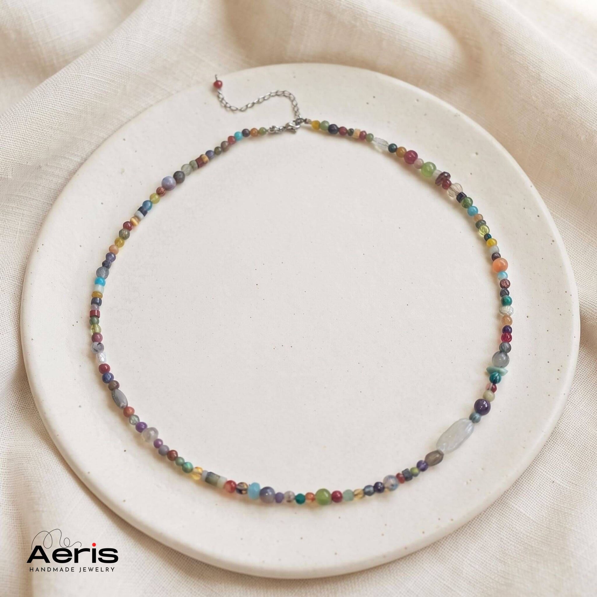 Colier handmade multicolor din margele naturale, expus pe un disc din ceramica mata