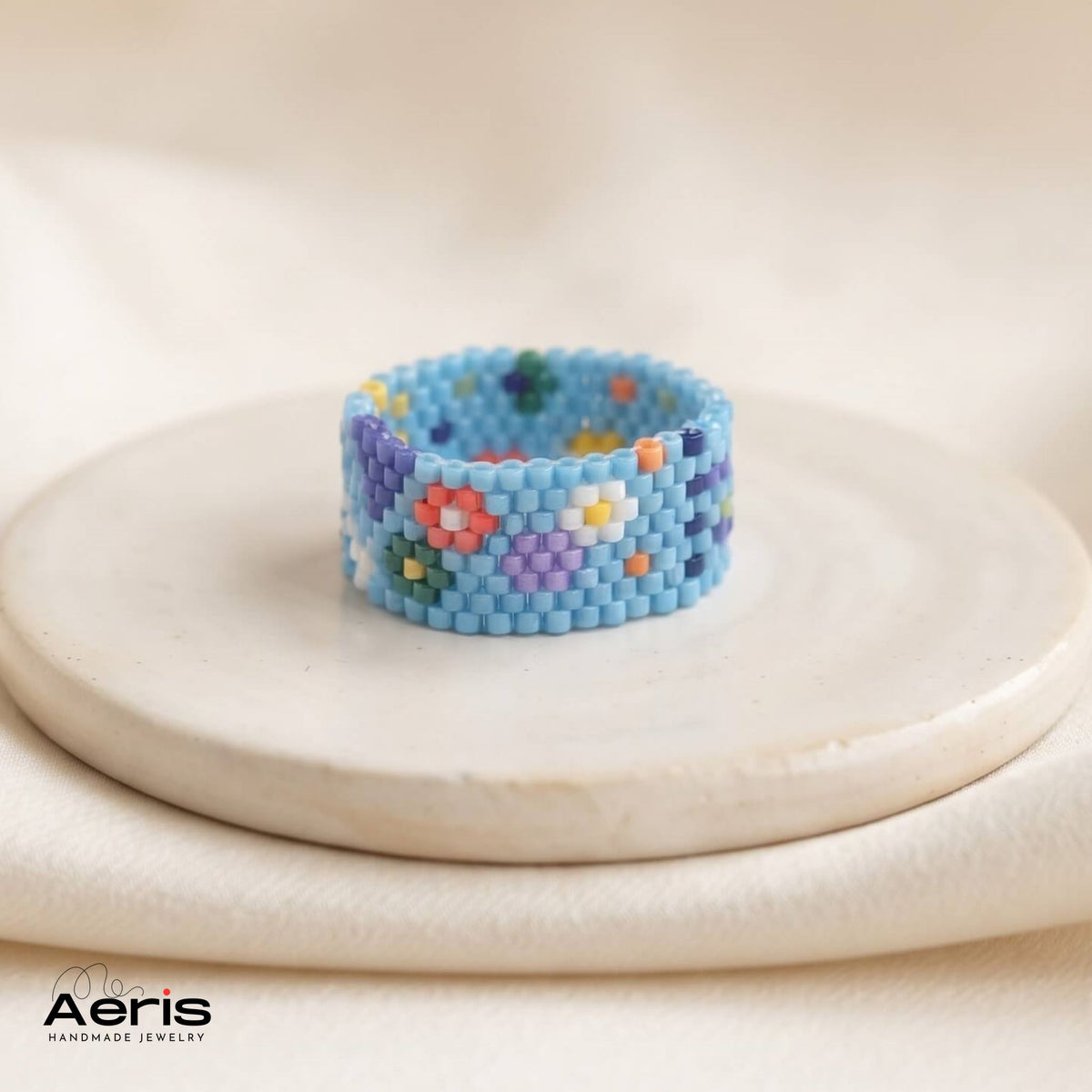 Inel handmade cu motive florale si geometrice, pe fond albastru deschis, asezat pe un disc ceramic