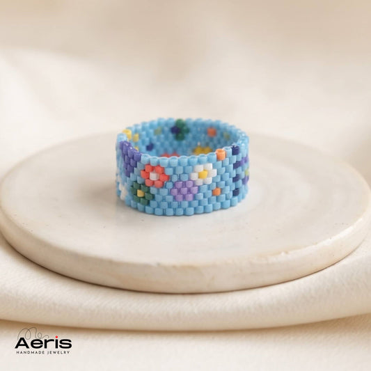 Inel handmade cu motive florale si geometrice, pe fond albastru deschis, asezat pe un disc ceramic