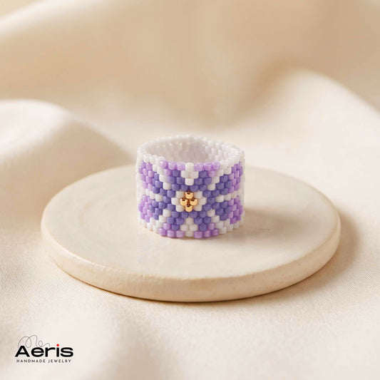 Inel handmade lat cu model floral din margele Miyuki, prezentat pe un disc de ceramica mata